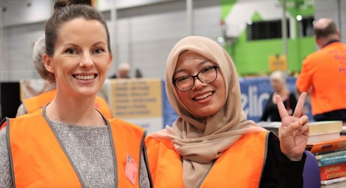 Two young women smile at the camera. Both are wearing hi-vis vests.