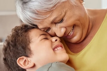 A close-up of a grandmother gently touching foreheads with her grandchild, both smiling warmly.