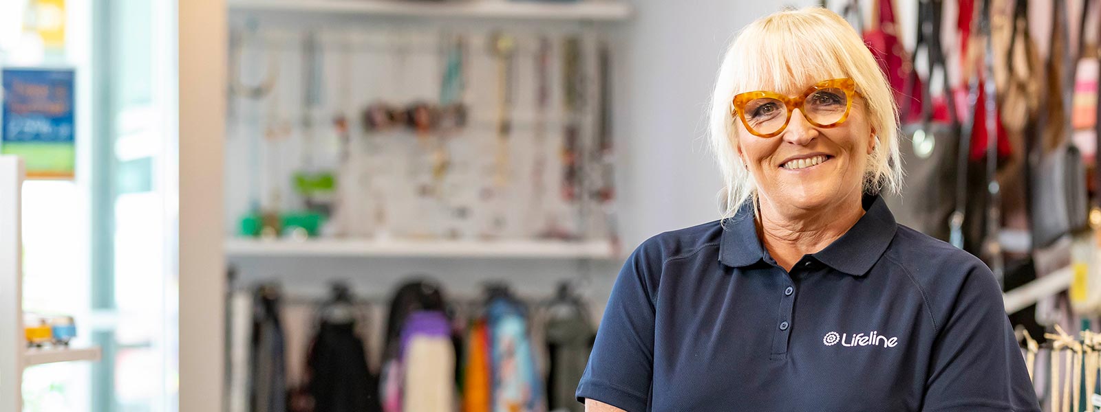 A smiling Lifeline employee stands in a Lifeline Shop in front of racks of clothing and other items.