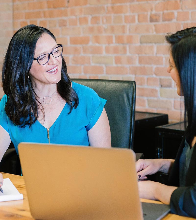 2 women conversing with a laptop on the table infront