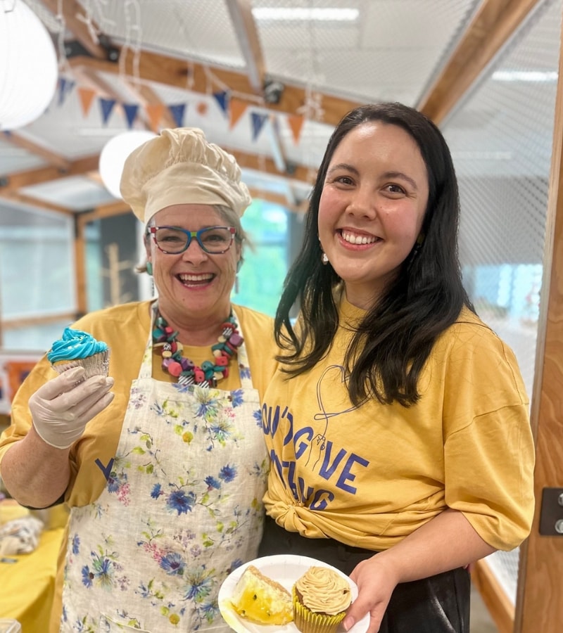 Two people dressed in yellow and blue are holding baked treats they're selling in their office to raise funds for Lifeline QLD