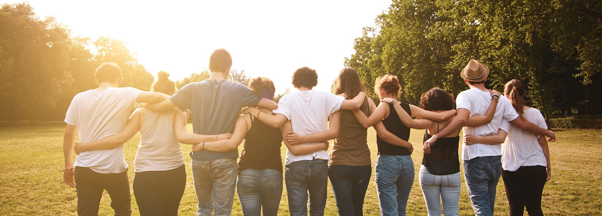 A group of 10 people walk into the sunset with their arms linked.