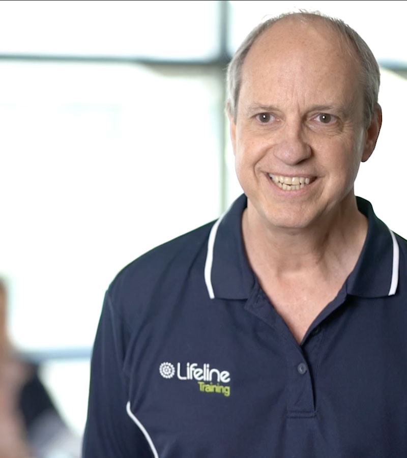 A Lifeline Training educator smiles as workplace training participants sit in the background.