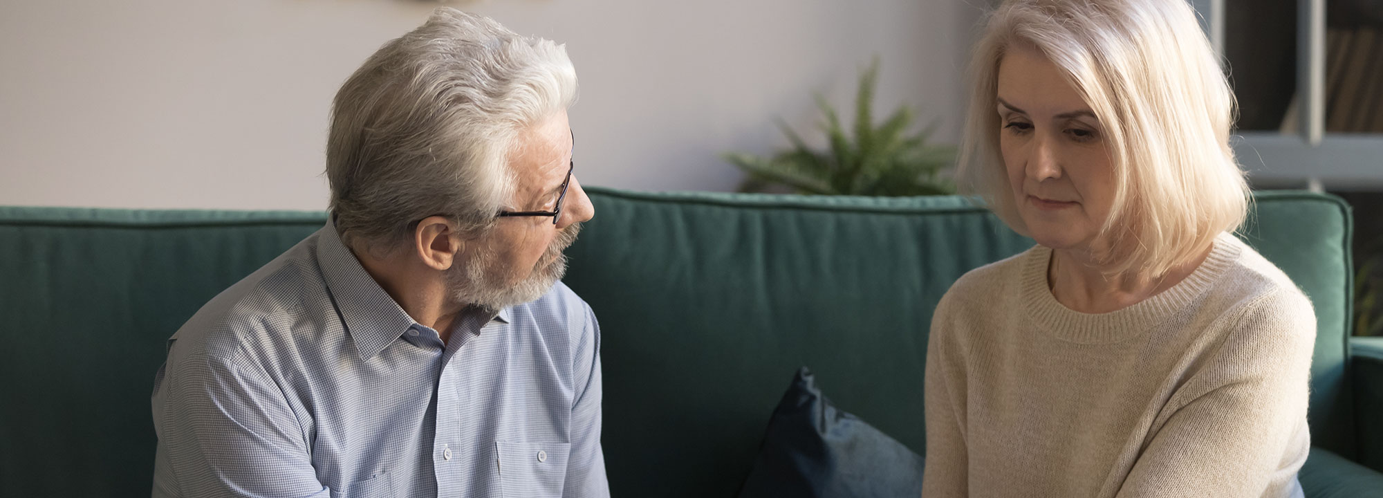 An older man and woman sit talking on a couch.